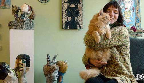 Artist-Laura-Jean-McLaughlin-hugs-Mojo,-one-of-four-cats-that-live-in-her-studio-and-gallery